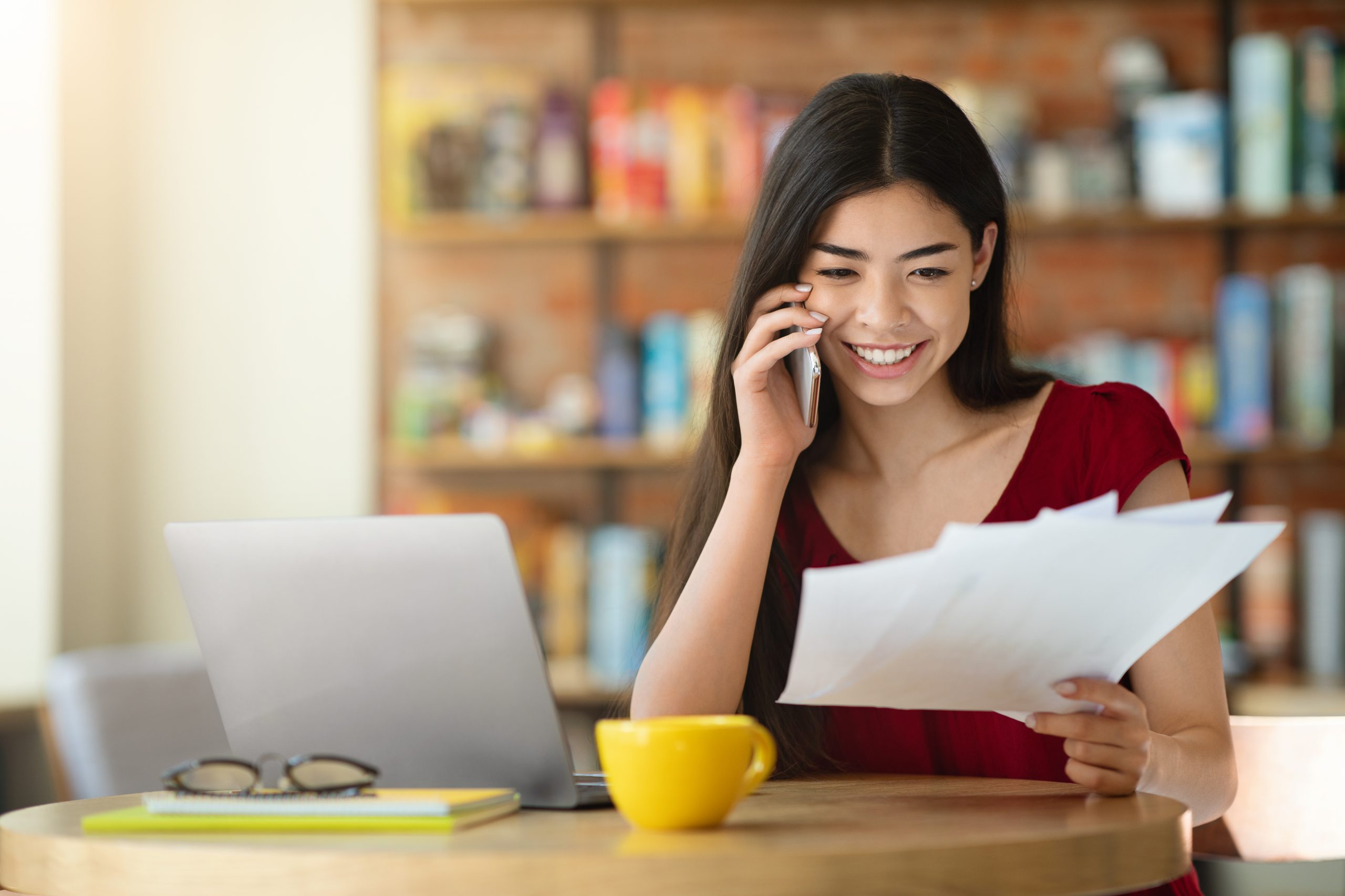 Remote Office. Asian Girl Checking Papers And Talking On Cellphone In Cafe